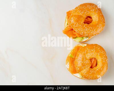 Due sandwich con salmone, formaggio cremoso, fette di cetriolo su un tavolo in marmo bianco, spazio per le copie, vista dall'alto Foto Stock
