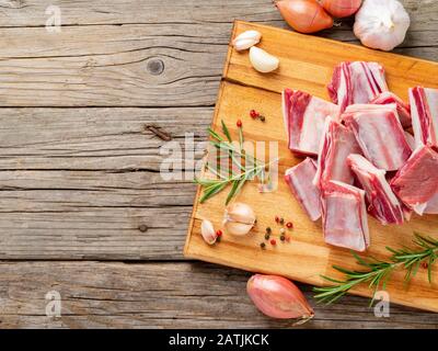 Piccoli pezzi di costolette di agnello crude su tagliere di legno su vecchio sfondo rustico di legno, vista dall'alto, copia spazio Foto Stock