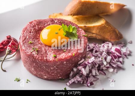 Tartare di manzo con tuorlo d'uovo cipolla rossa peperoncino peperoni erbe e bruschetta Foto Stock