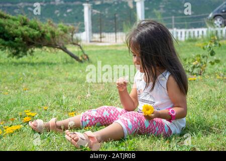 Ragazza piccola triste seduta sull'erba soffia dente di leone Foto Stock