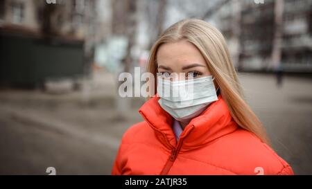 Giovane donna europea in una maschera protettiva dal coronavirus in città, concetto di inquinamento dell'aria e dell'assistenza sanitaria Foto Stock