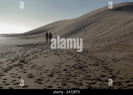 Una coppia tiene le mani mentre fanno una romantica passeggiata lungo la spiaggia accanto alle torreggianti dune di sabbia della Baia della Sardegna vicino a Port Elizabeth, Sud Africa Foto Stock