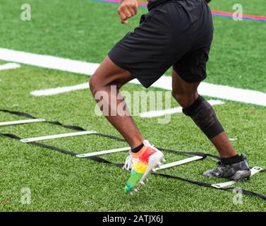 Un ragazzo di scuola superiore sta eseguendo esercizi a scala con scarpe colorate su un campo erboso durante le pratiche del campo estivo. Foto Stock