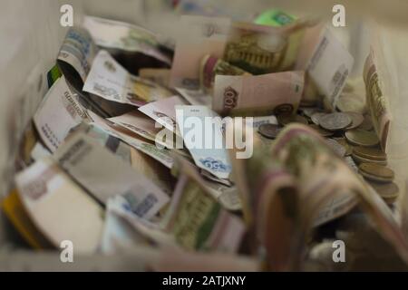 Rublo in valuta russa, monete metalliche e banconote in carta in una scatola per raccogliere donazioni di beneficenza. Raccolta fondi per la carità, il rublo e un penny Foto Stock