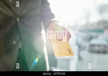 Primo piano di un uomo d'affari irriconoscibile che dà carta di credito durante il pagamento in negozio, effetto flare lente Foto Stock