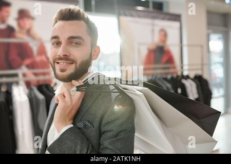 Ritratto di felice bel giovane uomo d'affari che porta borse di shopping a spalla mentre fa shopping in centro commerciale Foto Stock