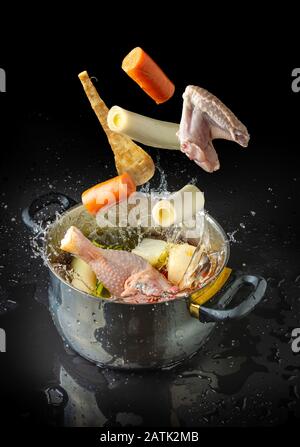 Ingredienti per fare il brodo volare verso un piatto con acqua spruzzata su sfondo nero Foto Stock
