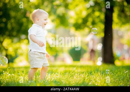 Ritratto bambino ragazzo che strisce fa il primo passo, cercando di alzarsi in piedi in parco Luce Del Sole Foto Stock