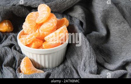 ancora vita, fette di mandarino maturo in un piatto bianco su uno sfondo di tessuto drappeggiato grigio Foto Stock