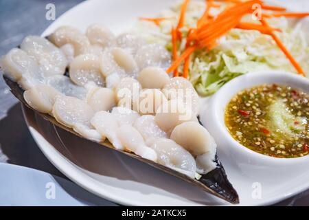 Pesce Fresco tailandese Selettivo: Sashimi di capesante a fette sottili con decorazione a guscio, servito con cavolo, carota e salsa piccante di pesce Foto Stock