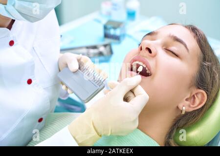 Bel sorriso e denti bianchi di una giovane donna. Abbinare le sfumature degli impianti o il processo di sbiancamento dei denti. Tavolozza dei denti. Foto Stock