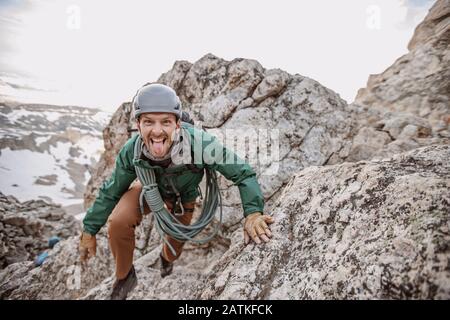 Scalatore di roccia maschio con corda e casco si stacca lingua fuori Foto Stock