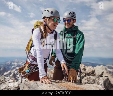 Coppia sorride con gioia dopo aver raggiunto la vetta del Grand Teton, Wyoming Foto Stock