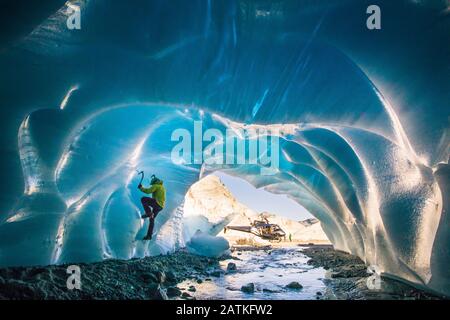 L'uomo ghiaccio sale all'interno della grotta glaciale durante il tour avventura in elicottero. Foto Stock
