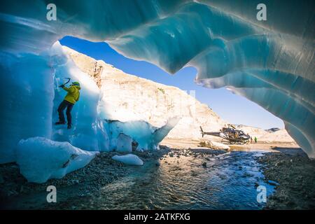 Uomo arrampicata su ghiaccio sul ghiaccio durante il tour avventura in elicottero Foto Stock