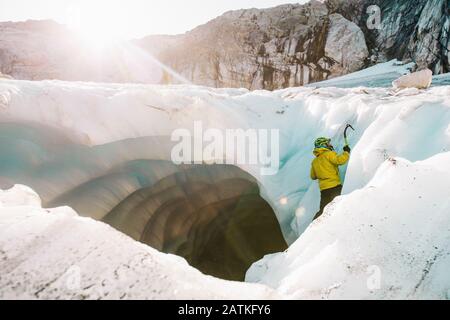 Vista laterale del ghiaccio dell'uomo che sale all'esterno della grotta glaciale. Foto Stock