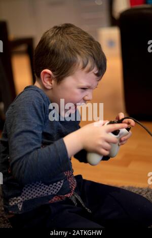 Piccolo ragazzo che gioca a console di intrattenimento elettronico con un controller bianco all'interno Foto Stock