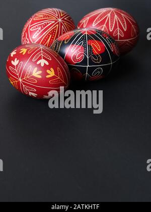 Gruppo di quattro tradizionali romeni rosso e nero dipinto uova di pasqua isolato su sfondo nero, orientamento ritratto, spazio di testo, fatto a mano Foto Stock