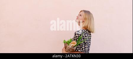 Zero sprechi. Ritratto di giovane donna in abito estivo con una carta artigianale eco sacchetto di verdure e baguette. Stile di vita sostenibile Foto Stock