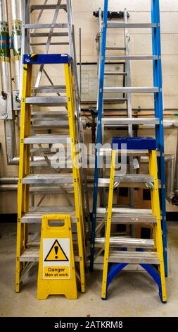 Vari set di scale e gradini in un laboratorio di manutenzione con un uomo in cantiere Foto Stock