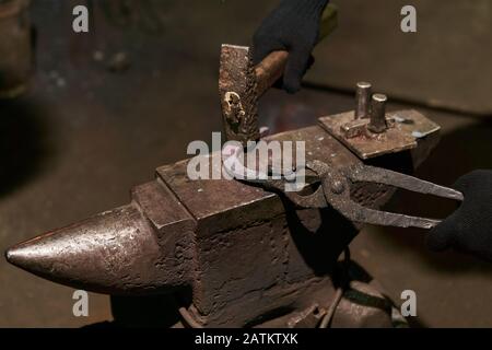 il fabbro forgia un ferro di cavallo sull'incudine con la forcella di piegatura, primo piano Foto Stock