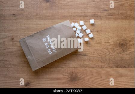 Cubetti di zucchero nella confezione di carta sul tavolo. "Gettare via, non mangiare" eccessivo zucchero presa di salute avvertimento sul pacchetto. Foto Stock