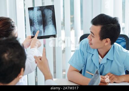 Fisiatristi e chirurgo ortopedico che discutono i raggi X del collo e della colonna vertebrale del paziente Foto Stock