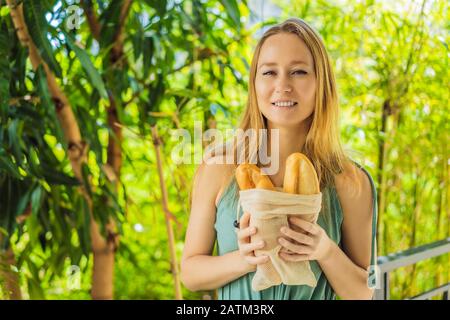 Sacchetti riutilizzabili di alimentari con pane nelle mani di una giovane donna. Zero sprechi shopping. Concetto di zero sprechi Foto Stock