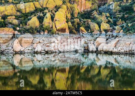 Basso livello dell'acqua, rocce bianchite e grandi massi ricoperti di licheni gialli riflessi sull'acqua al lago Bartlett, Arizona. Foto Stock