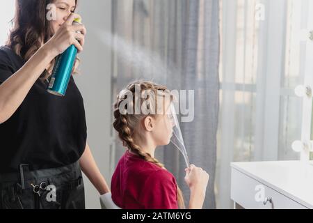 Il parrucchiere tessera una treccia ad una ragazza bionda pre-teen Foto Stock