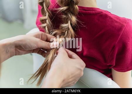 Il parrucchiere tessera una treccia ad una ragazza bionda pre-teen Foto Stock