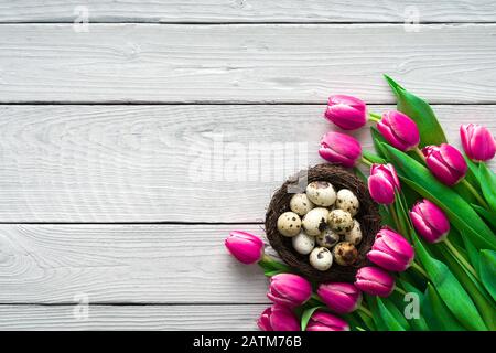 Bellissimi tulipani rosa con uova di quaglia in nido su sfondo di legno bianco. Concetto di vacanza di primavera e Pasqua con spazio di copia. Foto Stock