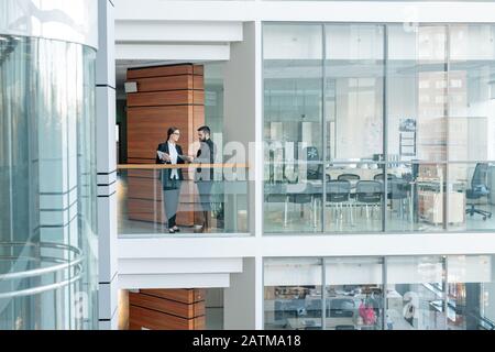 Giovani impiegati che si alzano sul balcone del centro affari e condividono idee per un nuovo progetto Foto Stock