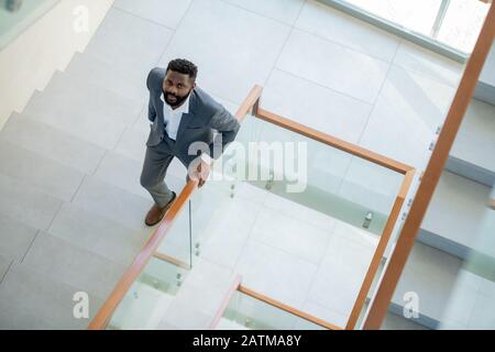 Vista ad alto angolo del serio uomo d'affari afro-americano sopportato in vestito che si muove su le scale e che guarda la macchina fotografica Foto Stock