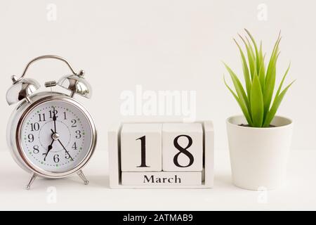 18 marzo su un calendario in legno accanto a un orologio di allarme e un fiore su uno sfondo bianco. Il concetto di un giorno per anno. Data O evento Significativo Foto Stock