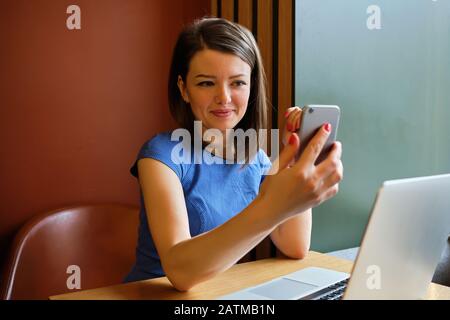 Una donna si trova in un bar di fronte a un computer portatile e fa una videochiamata e comunica. Primo piano. Foto Stock