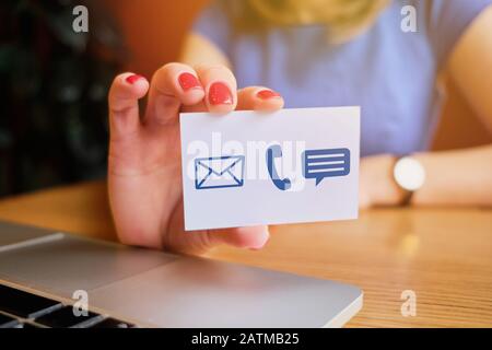 La ragazza tiene una carta bianca con icone astratte per la comunicazione - posta, telefono, messaggio. Primo piano. Foto Stock