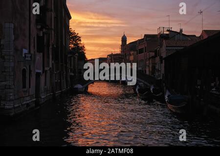 I tramonti la luce dorata si riflette nell'acqua di un pittoresco canale fiancheggiato da una gondola su Dorsoduro la sagoma di un ponte e ospita Venezia Italia Foto Stock