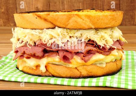 Panino in stile pastrami Reuben con crauti e formaggio svizzero su sfondo ligneo Foto Stock