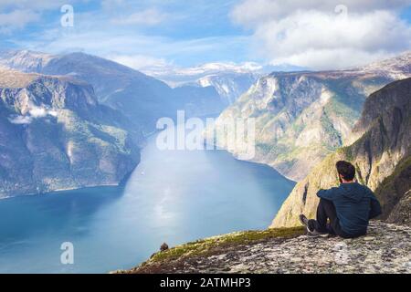 Uomo seduto sul bordo della scogliera da solo godendo vista aerea backpacking stile di vita viaggio avventura all'aperto vacanze estive in Norvegia cima a bello Foto Stock