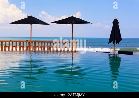 Piscina a sfioro con bar sulla spiaggia, ombrelloni e lettini. Splendida vista sul mare surf con surfisti a cavallo sulle onde. Stile di vita sano Foto Stock