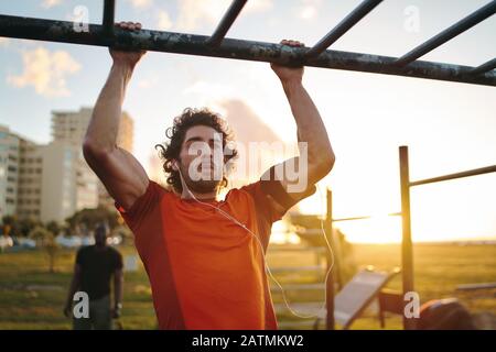 Ritratto di un giovane sportivo crossfit che si esercita sul bar, facendo tiri per braccia e muscoli posteriori al parco esterno della palestra Foto Stock