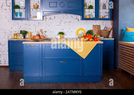 Interni moderni in stile loft con cucina blu e mobili. Tavolo vuoto in legno e giallo primavera decor in cucina interno. Scandinavo Elegante Foto Stock