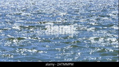 Troppi riflessi luminosi del sole sulla superficie dell'acqua di mare. Primo piano del mare con piccole increspature in una giornata di sole. Foto Stock