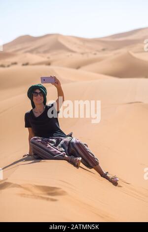 Ragazza che prende un selfie nel deserto con un turbante sulla sua testa. Foto Stock