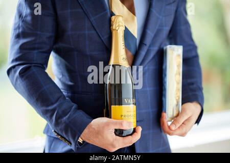 Uomo che tiene una scatola di cioccolatini e una bottiglia di vino Foto Stock