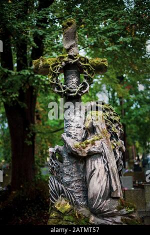 Vecchia scultura in pietra tombale di una donna che abbraccia una croce nel cimitero storico di Rakowicki a Cracovia, Polonia Foto Stock