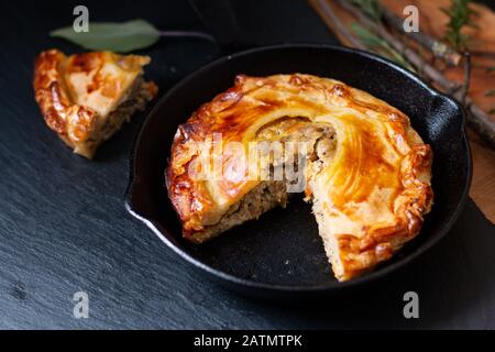 Concetto di cibo fatto in casa torta di pasta sfoglia di carne dorata in padella ghisa su lavagna di ardesia nera con spazio copia Foto Stock