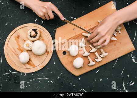 Funghi Champignon su una tavola di legno. Tagliare i funghi per preparare piatti deliziosi per la cena. Funghi freschi tritati Foto Stock