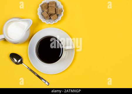 Una tazza di caffè con una cameriera e cubetti di zucchero di canna su sfondo giallo Foto Stock